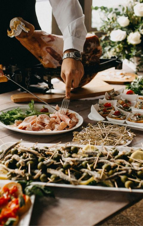 A chef slices meat in a beautifully arranged catering setup with diverse appetizing dishes.