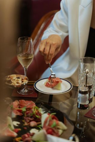 Person enjoying prosciutto and wine at an upscale restaurant.