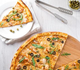 High-angle view of pizza topped with olives, arugula, and cheese. A mouthwatering slice on a plate nearby.